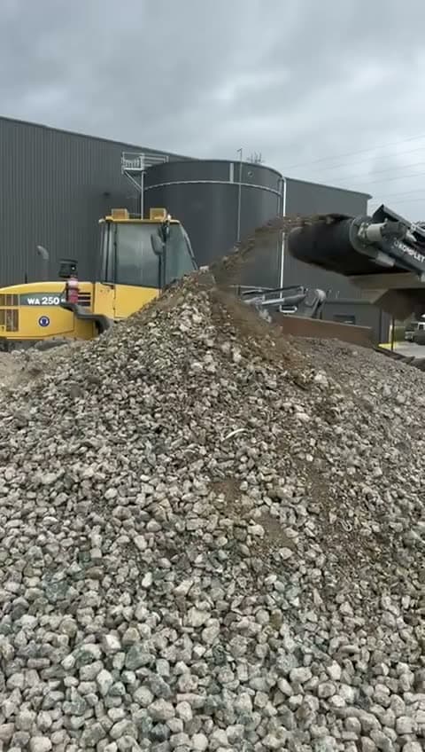 Crushed rock discharging onto a stockpile with a Komatsu WA250 loader behind